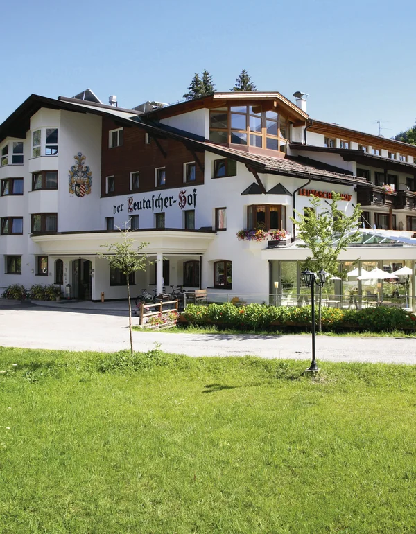 Großes Hotelgebäude mit Terrasse und grüner Wiese im Vordergrund