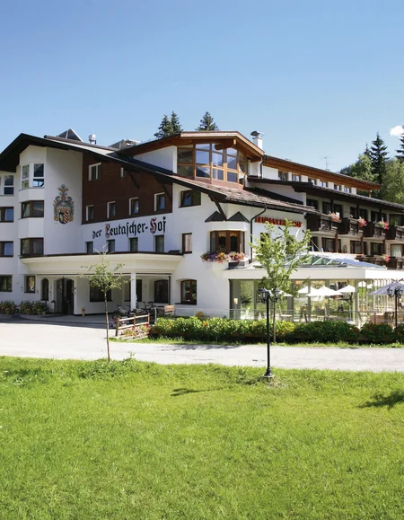 Großes Hotelgebäude mit Terrasse und grüner Wiese im Vordergrund