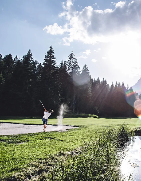 Ihr Sporthotel in Tirol Person spielt Golf auf grünem Golfplatz mit Bergen und Wald im Hintergrund