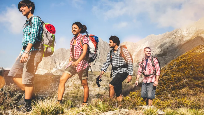 Gruppe von vier jungen Wanderern mit Rucksäcken in den Bergen bei sonnigem Wetter