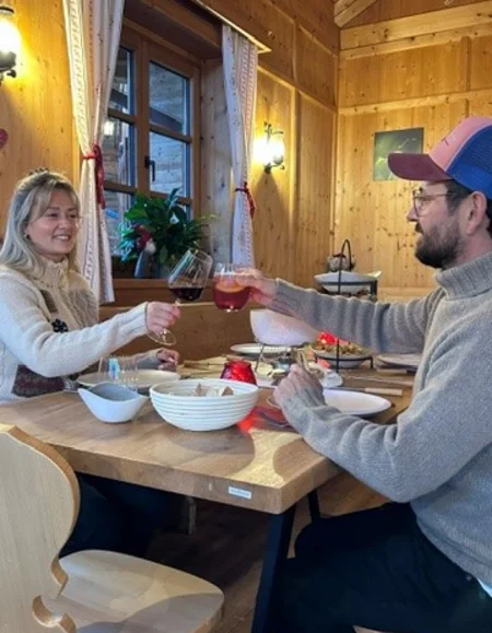 Paar stößt mit Getränken an in einer gemütlichen Holzhütte beim Essen