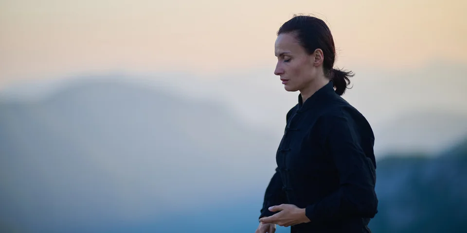 Frau meditiert im Freien vor einem nebligen Bergpanorama bei Sonnenaufgang