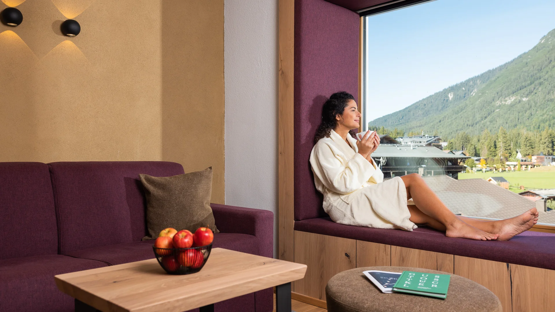 Biohotel Leutascherhof – Ihr Kraftort in den Tiroler Alpen Frau im Bademantel sitzt am Fenster und genießt Ausblick auf Berge