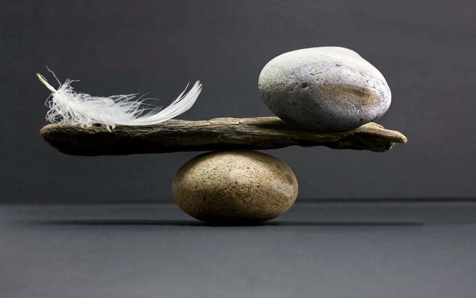 Feder und Stein balancieren auf Holzstück und rundem Stein auf grauem Hintergrund