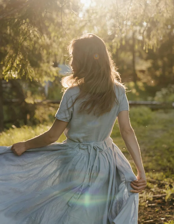 Frau im blauen Kleid dreht sich im Sonnenlicht in der Natur