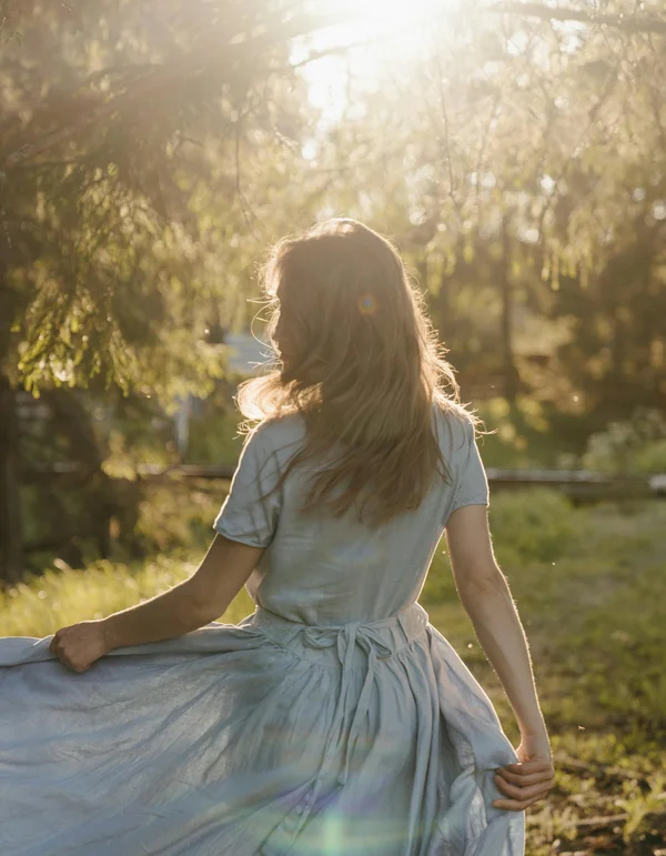 Frau im blauen Kleid dreht sich im Sonnenlicht in der Natur