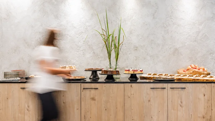 Das Hotel mit Bio-Küche in Tirol unscharfe person vor buffet mit kuchen und obst auf holztheke
