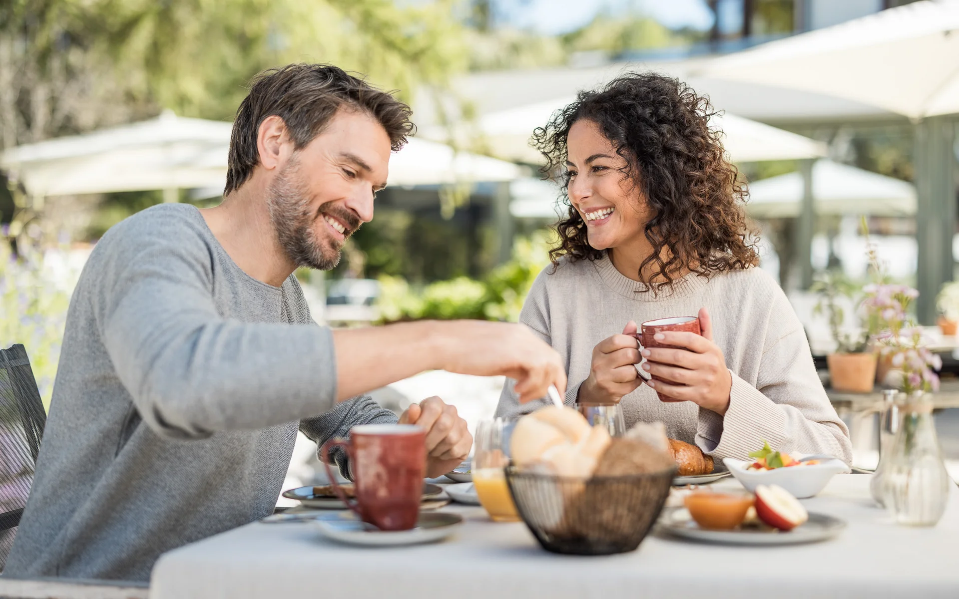 Werfen Sie einen Blick in die Bildergalerie Paar genießt Frühstück im Freien mit Kaffee und Brötchen am Tisch