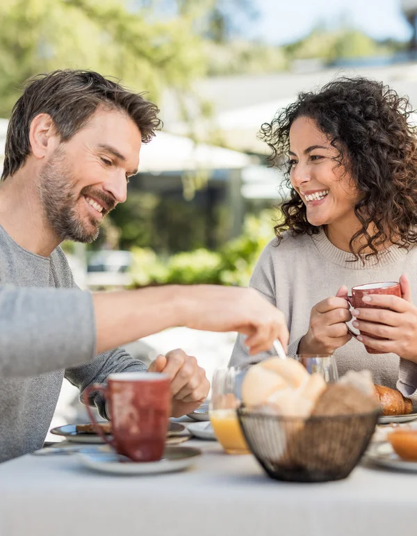 Paar genießt Frühstück im Freien mit Kaffee und Brötchen am Tisch