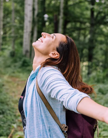Frau mit ausgestreckten Armen genießt die Natur im Wald