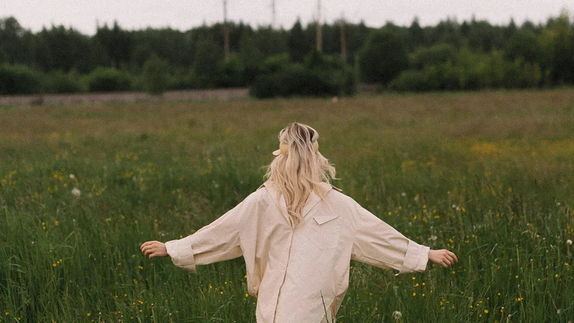 Person geht mit ausgestreckten Armen durch eine Blumenwiese