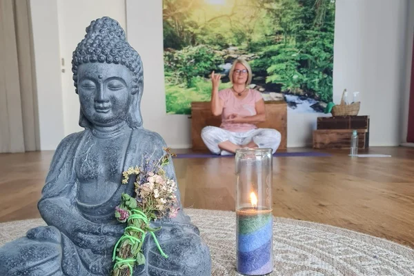 Buddha-Statue mit Kerze und Frau im Meditationsraum im Hintergrund