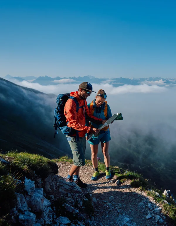 Zwei Wanderer mit Karte auf einem Bergweg über den Wolken