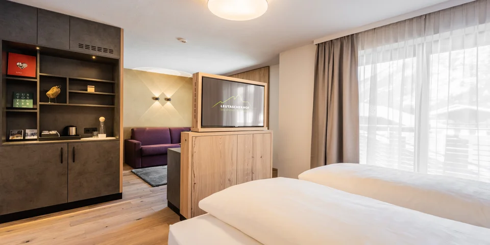 Modernes Hotelzimmer mit zwei Betten, TV und Blick auf den Vorraum mit Sofa