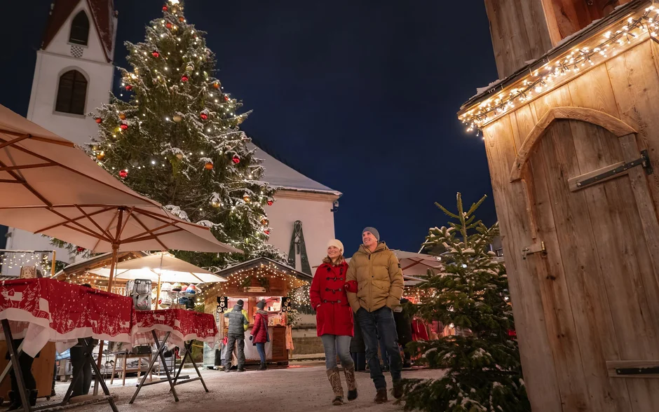 Paar auf einem winterlichen Weihnachtsmarkt mit beleuchtetem Weihnachtsbaum und Marktständen