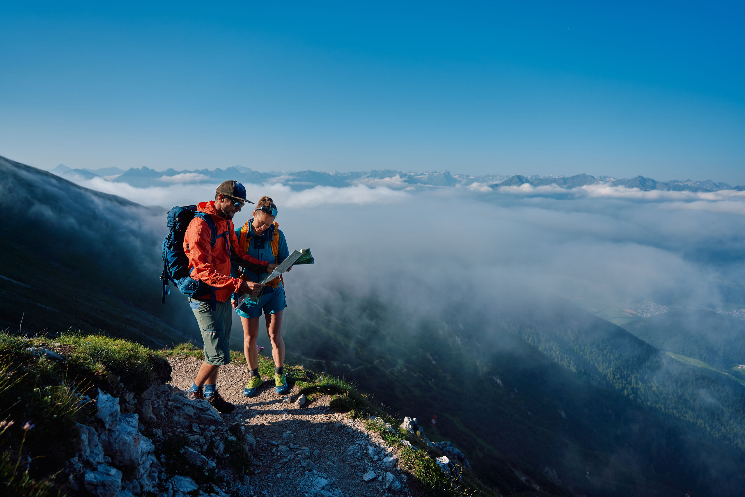 Werfen Sie einen Blick in die Bildergalerie Zwei Wanderer mit Karte auf einem Bergweg über den Wolken