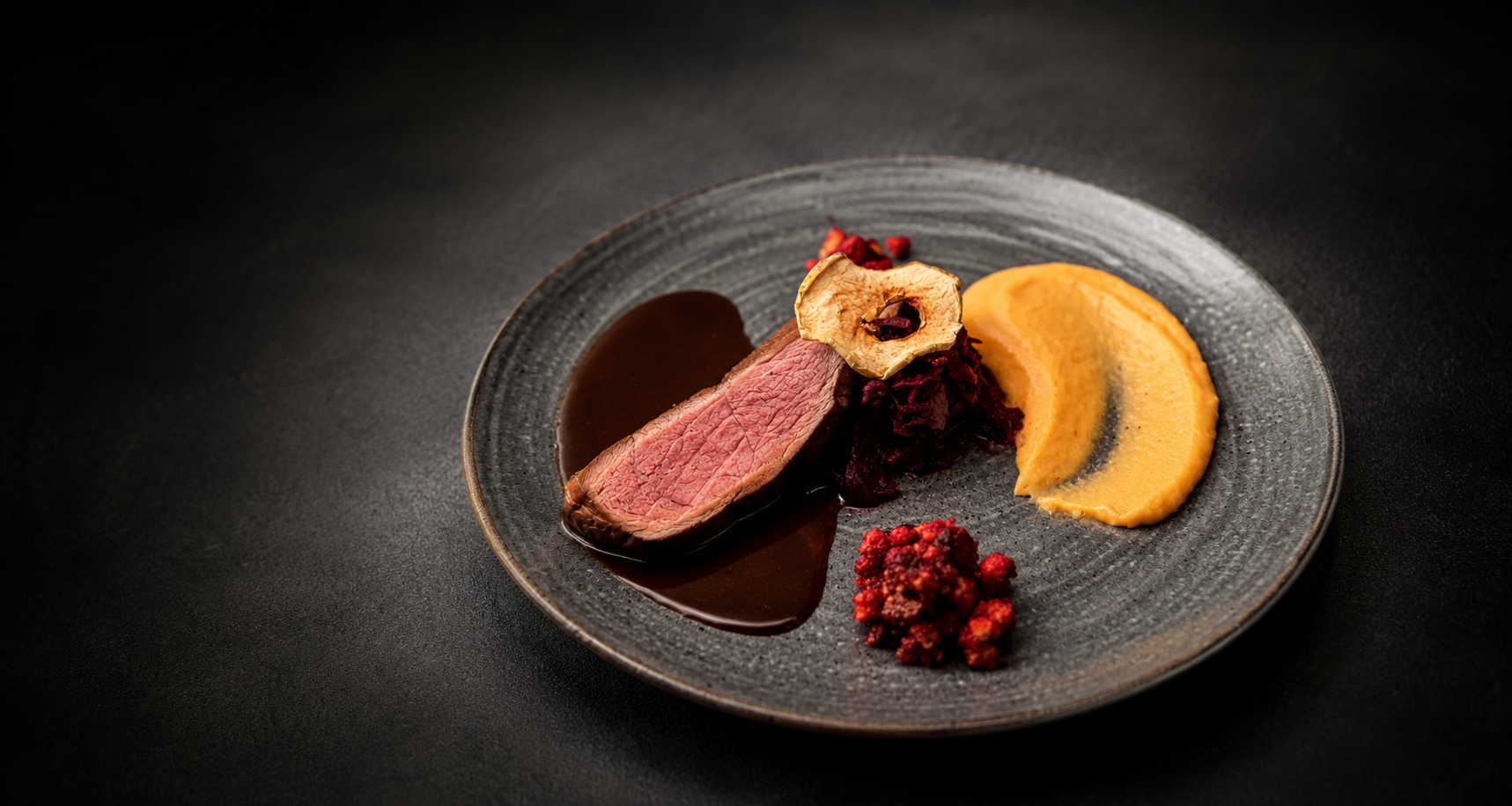 Ein Teller mit rosa gebratenem Fleisch, dunkler Sauce, Gemüsepüree und Beeren